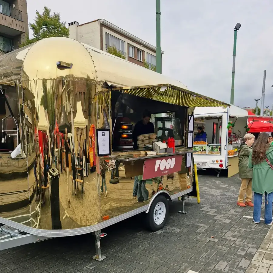 Gleaming golden Airstream food truck with a pizza oven on a town square
