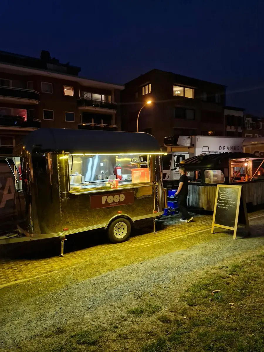 Golden Airstream food truck in the evening, lit with yellow light, in front of an apartment block