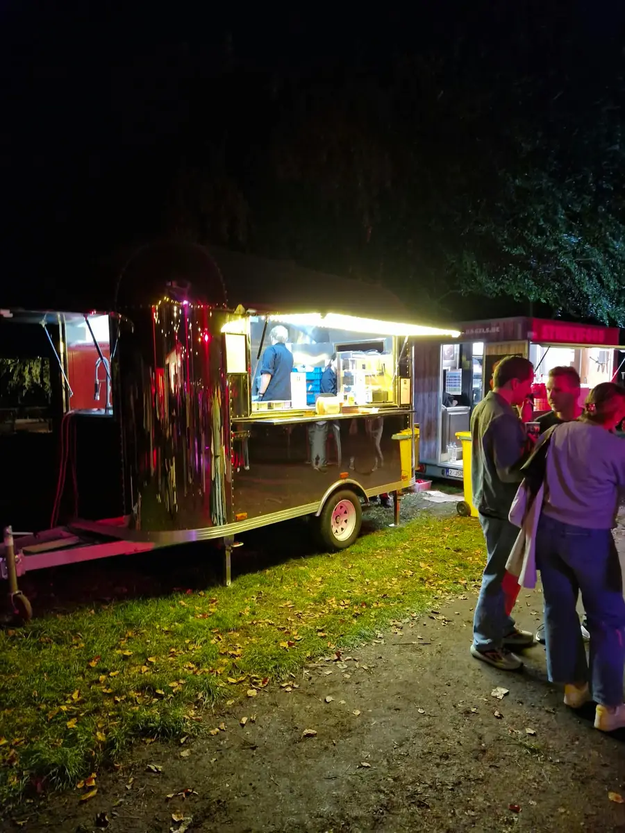 Illuminated food truck in the dark with visitors gathered at the serving hatch
