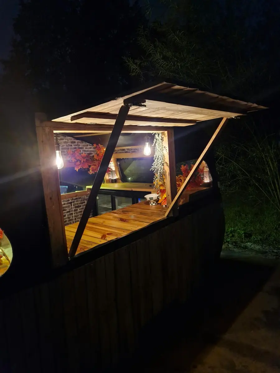 Wooden caravan bar with its serving hatch open, warmly lit in the dark