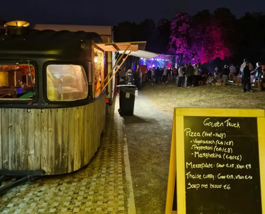 A vintage wooden caravan at dusk next to a chalkboard, with party guests in the background