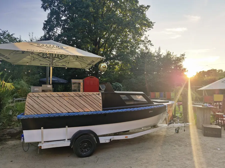 A boat converted into a bar on a trailer, in the sunlight under the trees