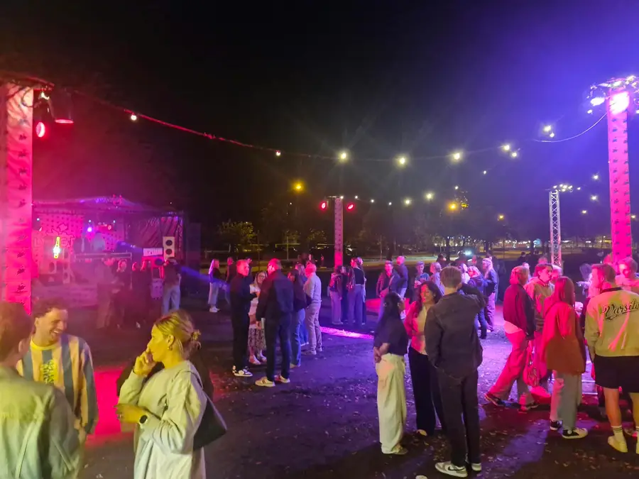 Partygoers dancing in the evening under string lights with pink and purple lighting