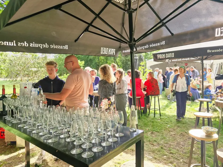 Garden party with a bar full of glasses and guests under the trees and parasols