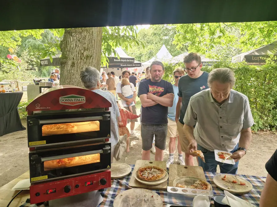 Pizzas baking in a small pizza oven at an outdoor party, with guests queuing up